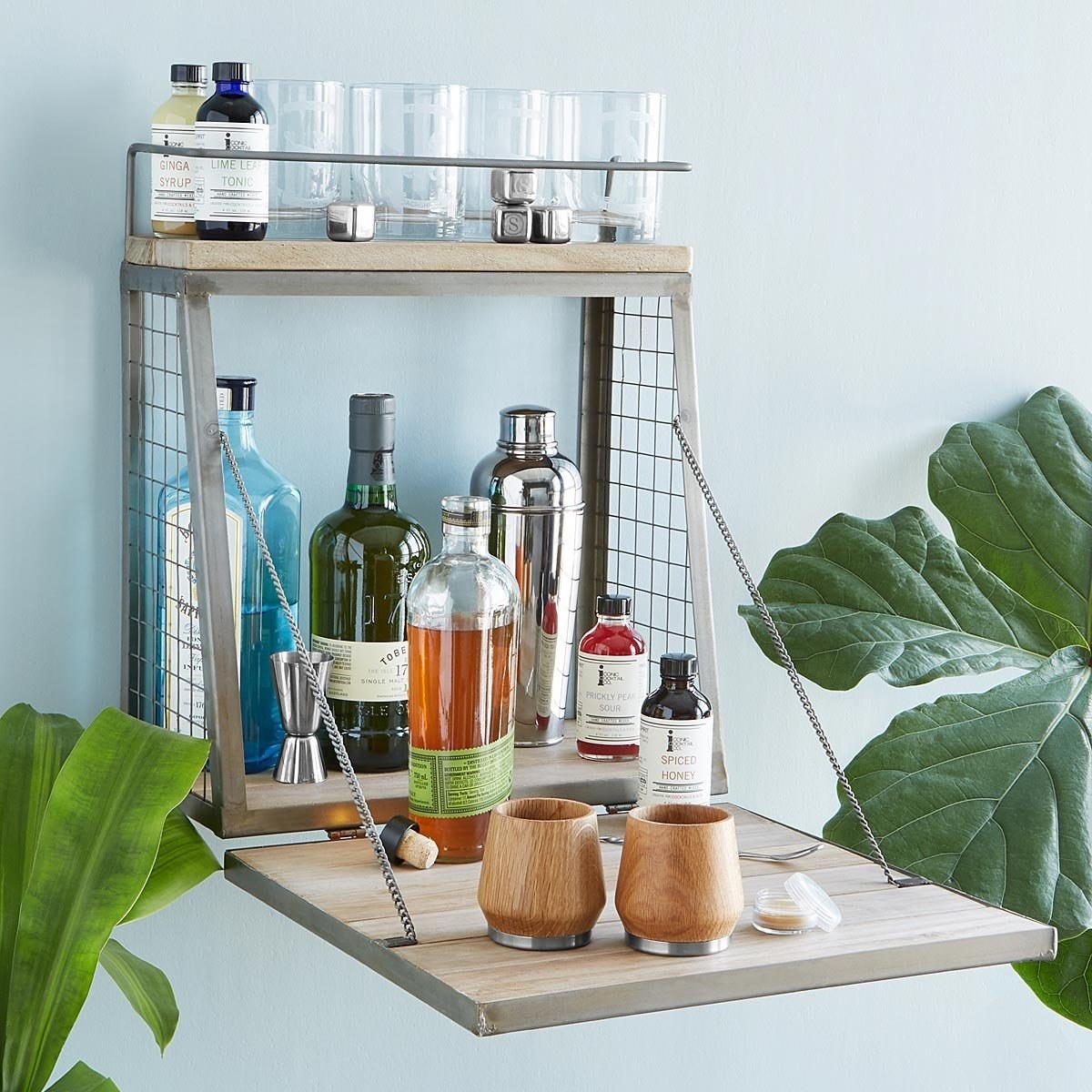 The wall-mounted fold-down shelf loaded with alcohol bottles and glasses