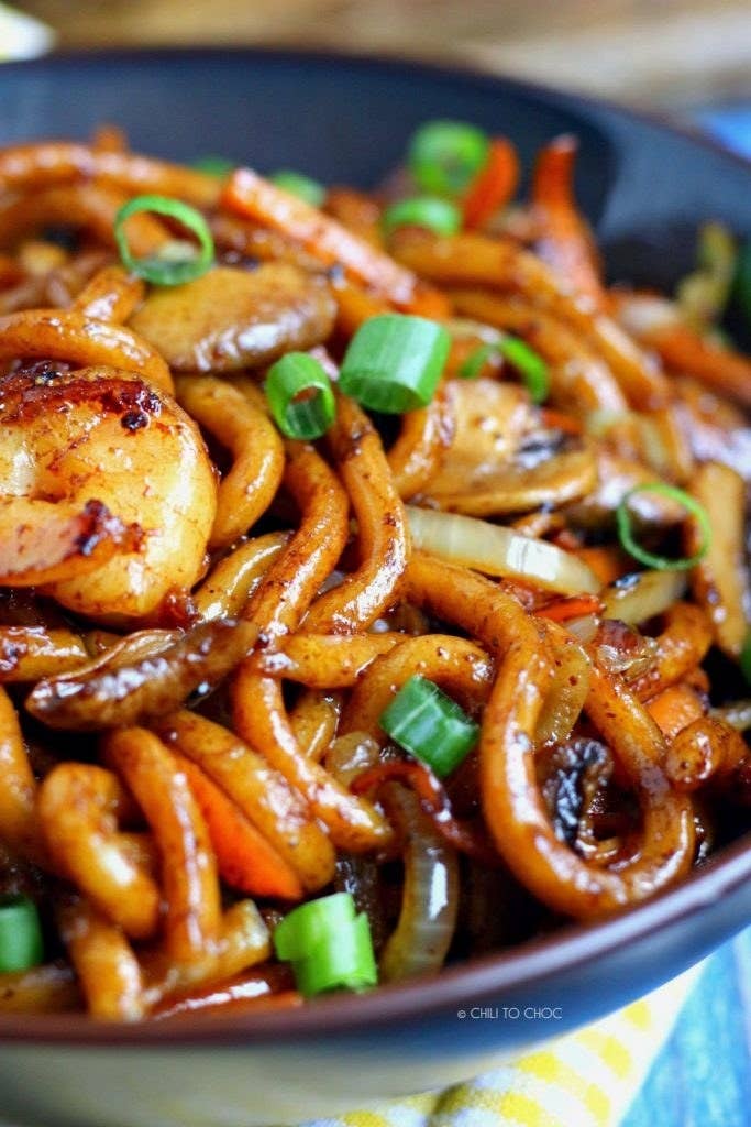 A bowl of udon noodle stir fry with carrots, mushrooms, and scallions tossed in soy sauce.