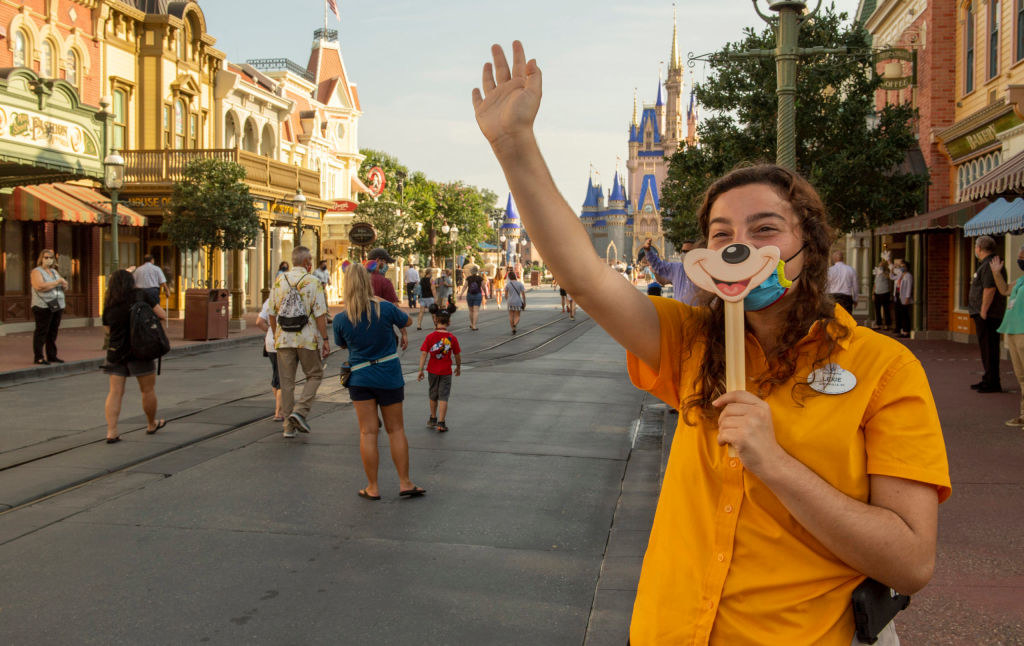 A worker holds a Mickey Mouse smile sign over her face mask