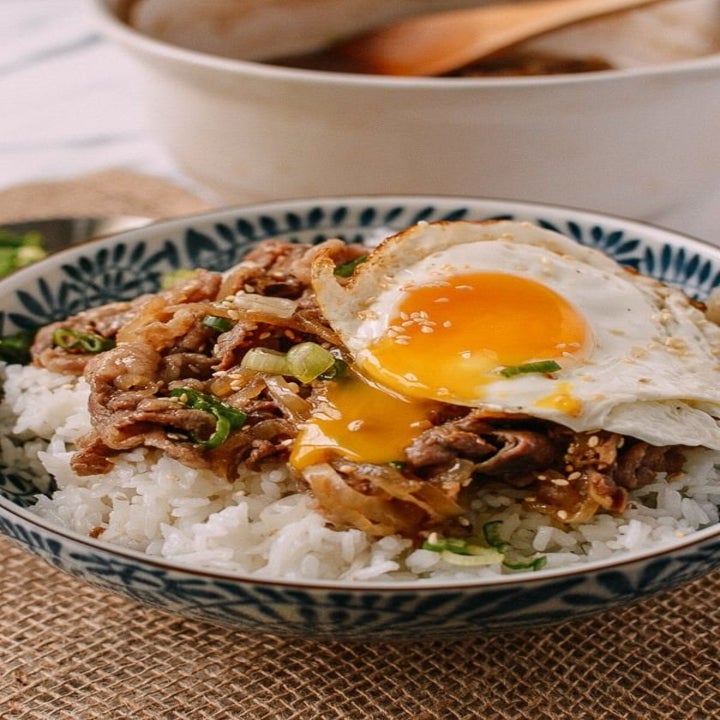 A runny egg on top of a Japanese beef and rice bowl.