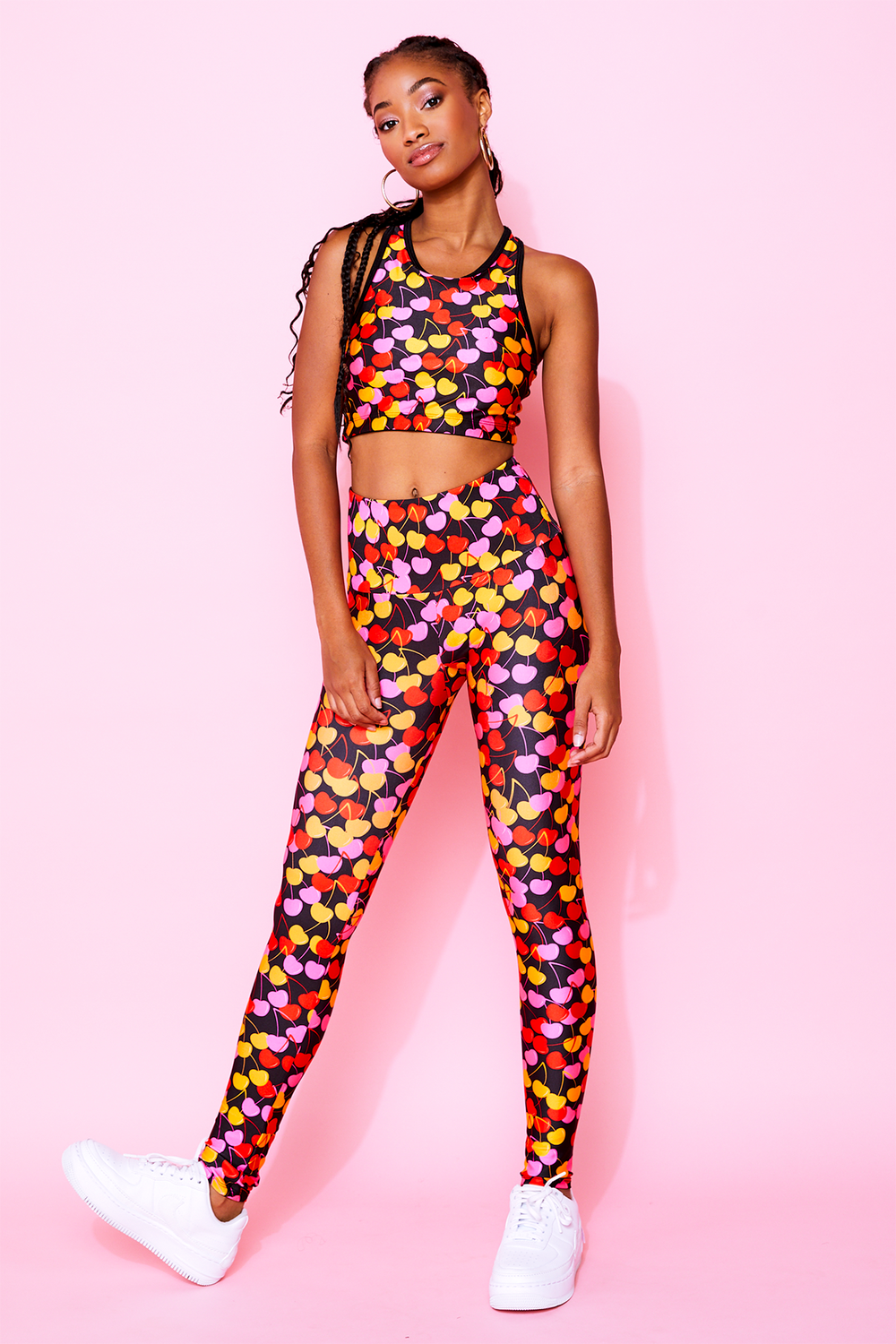 Model wearing high-waisted full-length leggings in black with yellow, pink, and red cherries all over