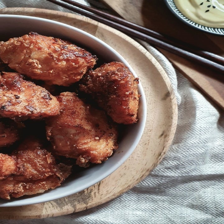 A bowl of golden brown fried chicken with chopsticks and mayo dipping sauce on the side.