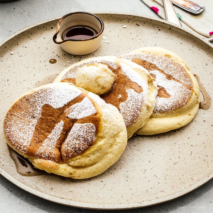 Three fluffy Japanese pancakes on a plate topped with powdered sugar and syrup.