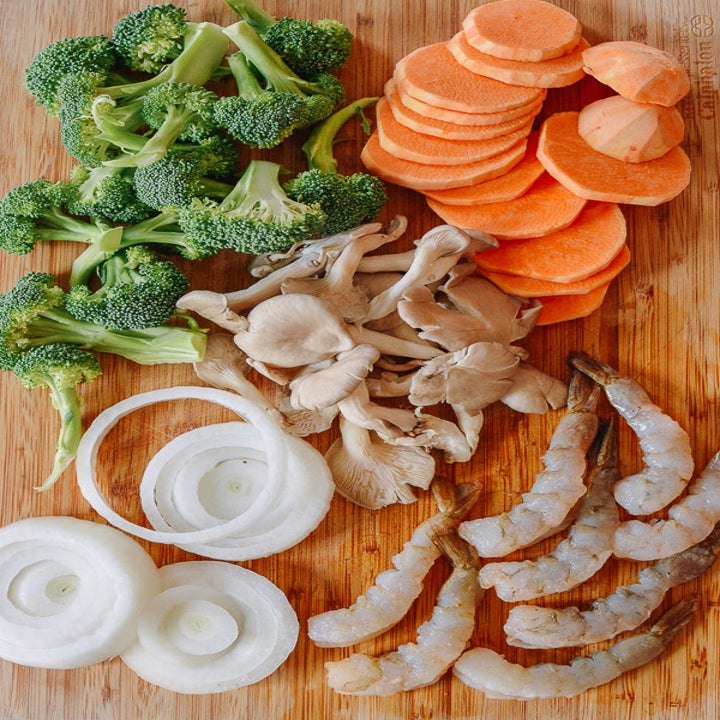 Broccoli, carrots, onion, mushrooms, and shrimp for tempura on a cutting board.