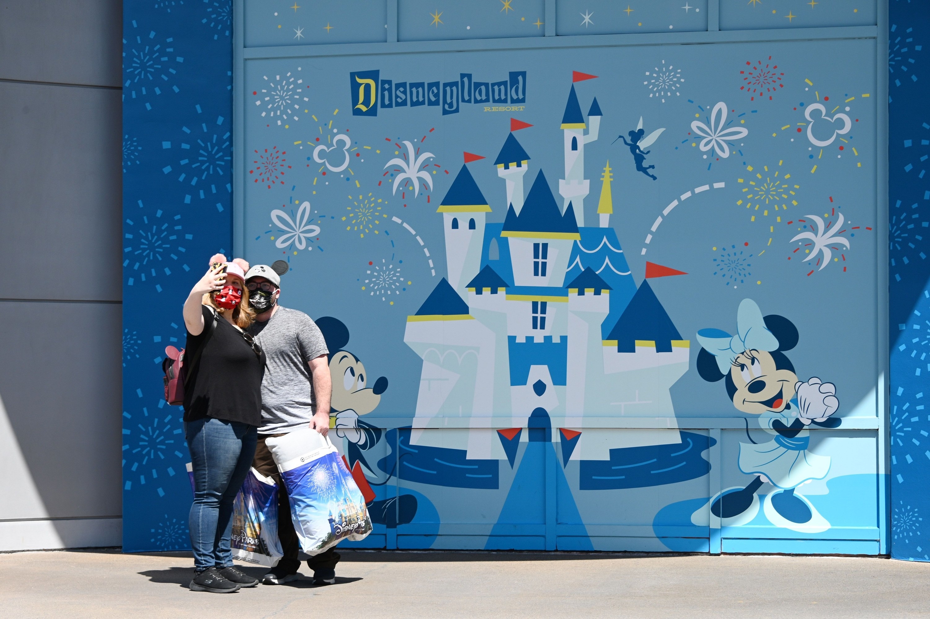 Two people take a selfie in front of a Disneyland mural