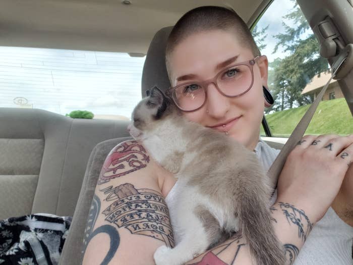 Taylor sits in a car with a recently adopted kitten named Zucchini resting on their shoulder