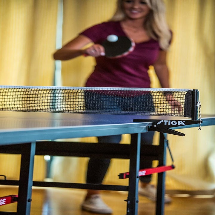 A close up view of the net on the ping pong table with a model playing in the background