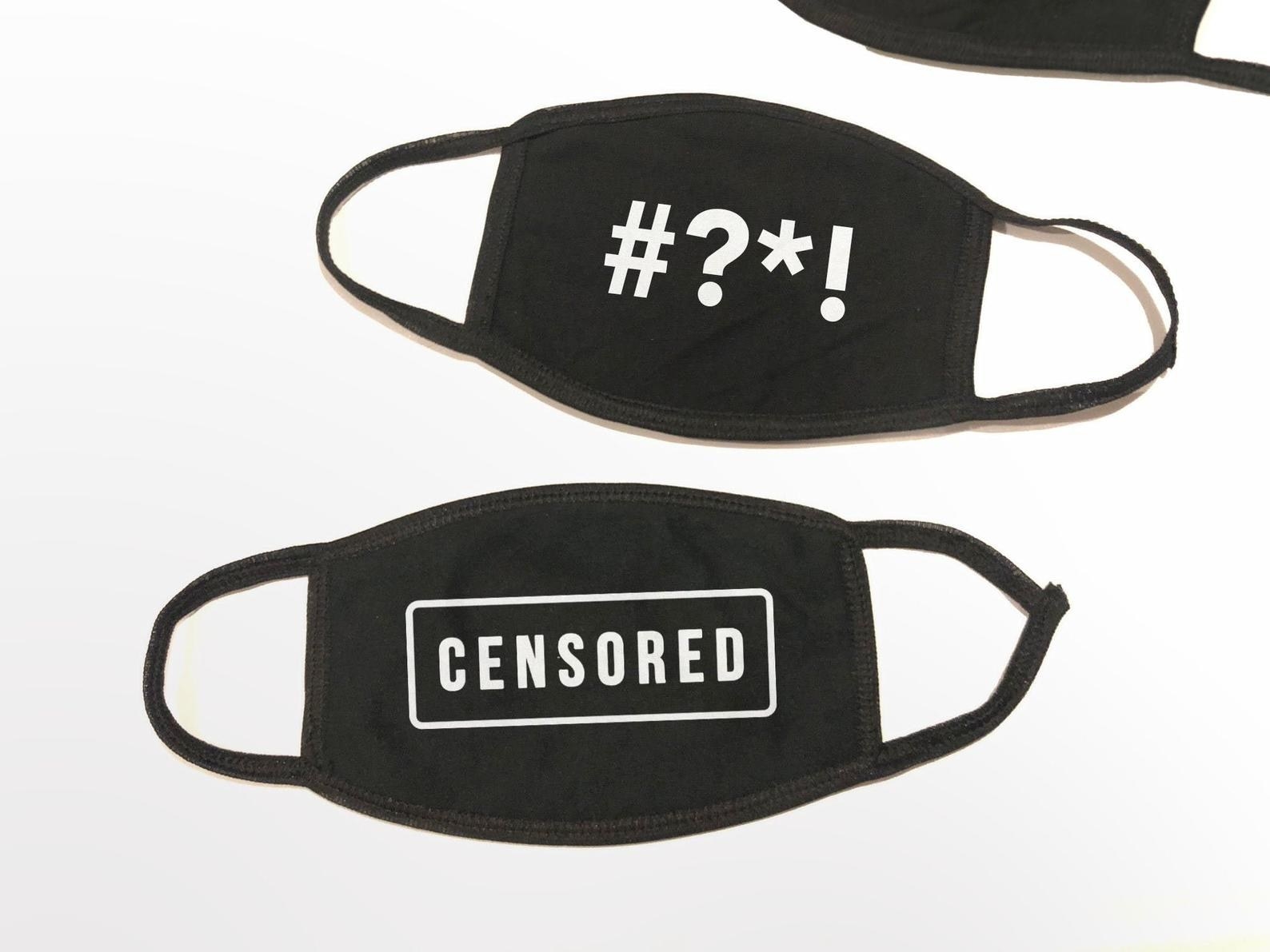 Two black masks, one that says CENSORED and another that says #?*! like a bleeped out swear word 