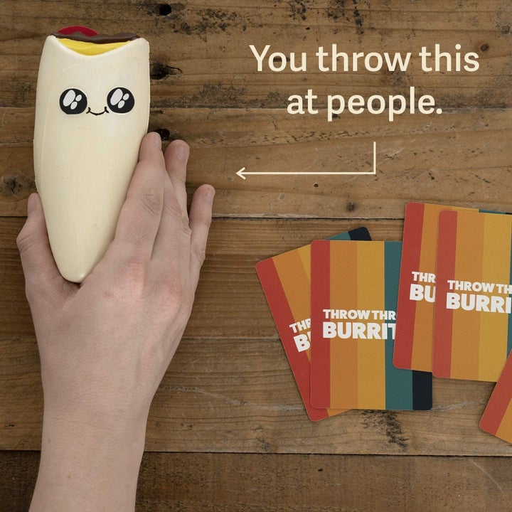 A model's hand holding a toy burrito and playing cards
