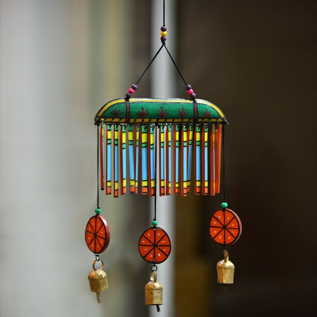 Wooden wind chimes painted in blue, green, yellow and orange. The ends have wooden orange slices and bells hanging on them.