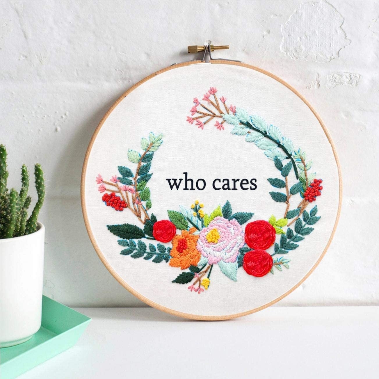 An embroidery hoop with a finished piece that has flowers around the words "who cares"