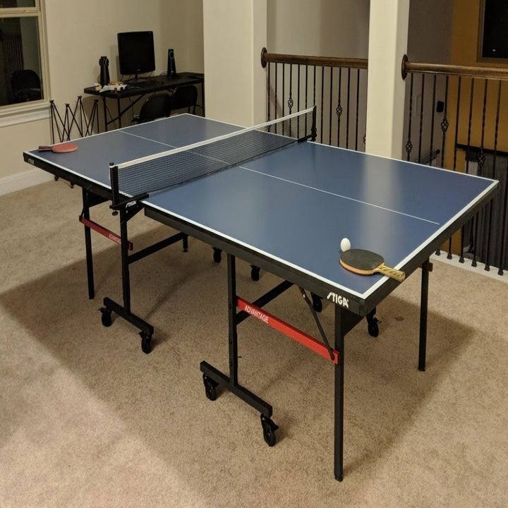 A blue ping pong table with black legs and wheels and red accents