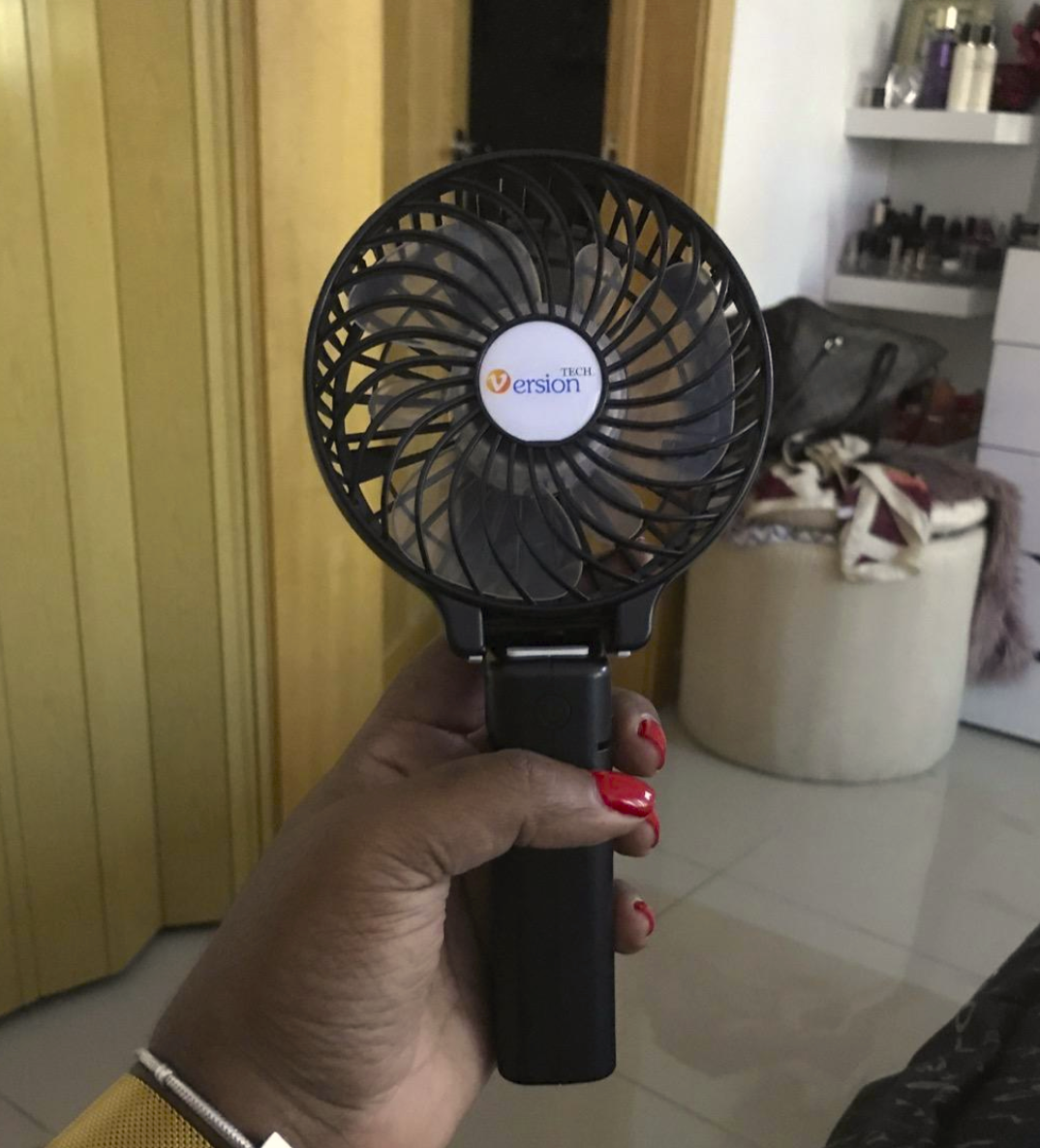 reviewer&#x27;s hand holding the fan which is circular on the fan end has a handle 