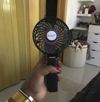 reviewer's hand holding the fan which is circular on the fan end has a handle 