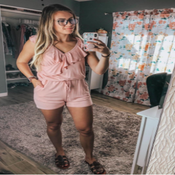 A reviewer wearing the sleeveless, tie-waist romper in pale pink
