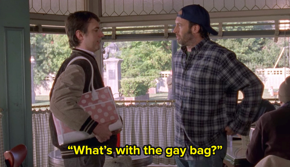 Luke and Kirk from Gilmore Girls stand in a diner. Kirk carries a pink bag and Luke asks him what&#x27;s with the gay bag?