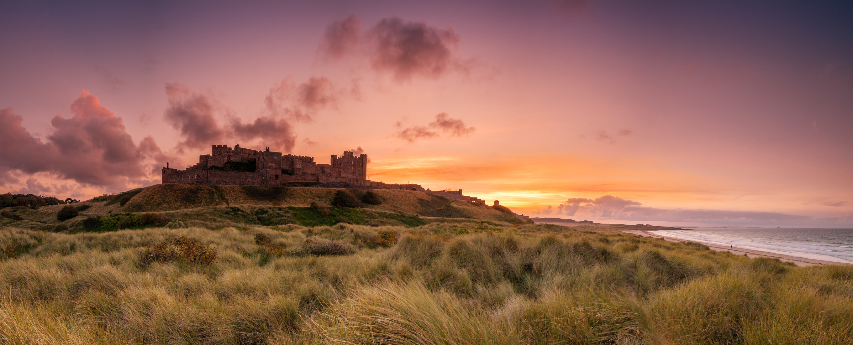 A pink and gold sunset view across Bamburgh castle and the beach in Northumberland