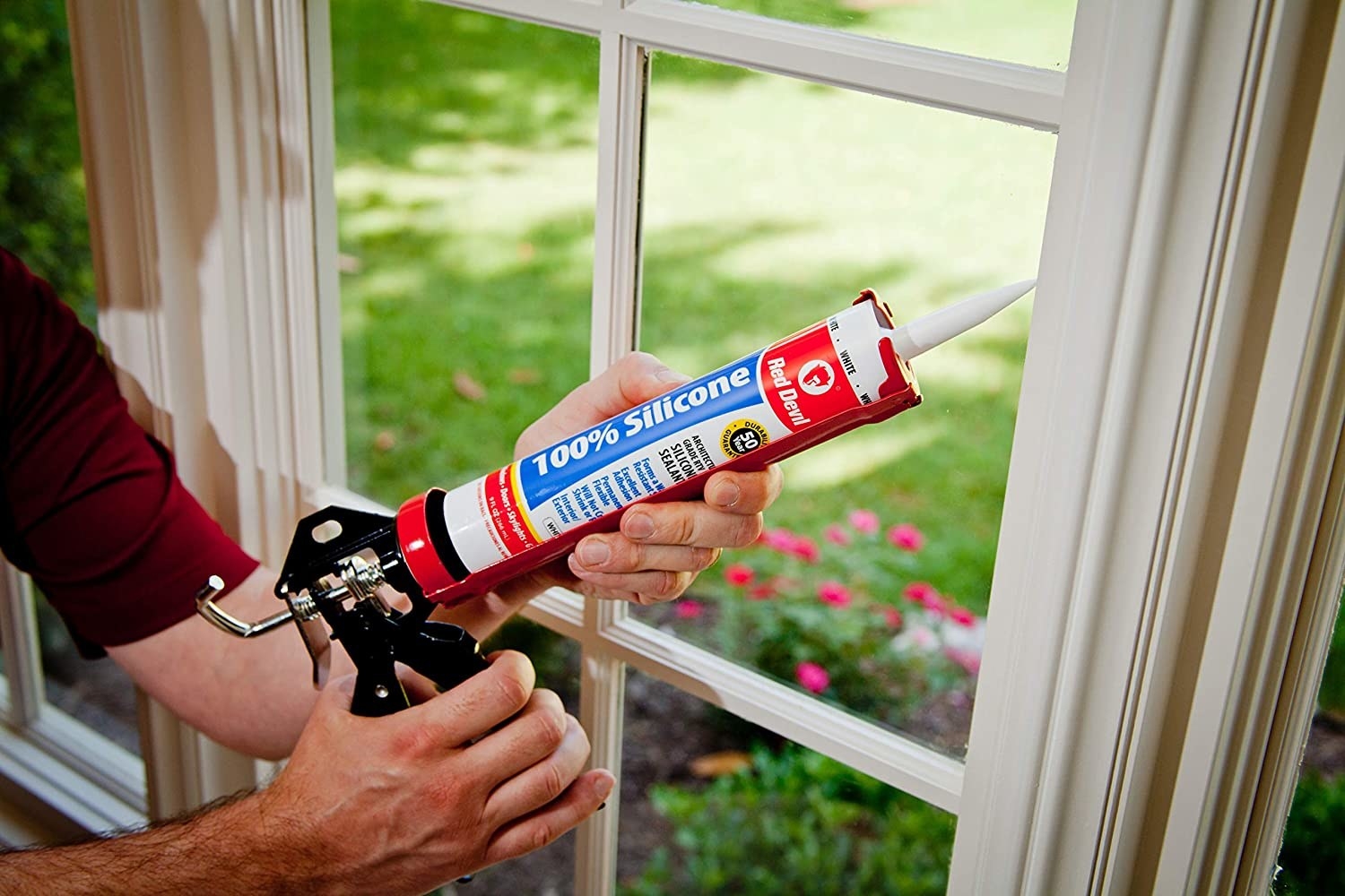 A person fixing a window frame with the caulking gun