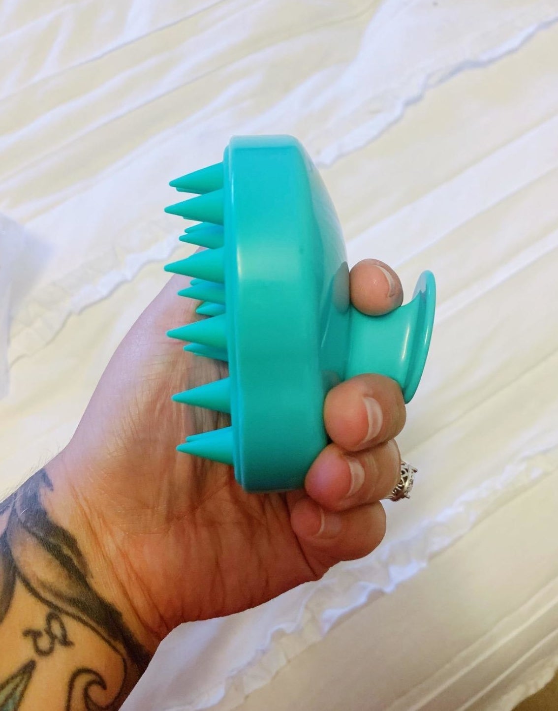 reviewer holding teal silicone brush with soft massaging spikes on one side and a small handle on the other