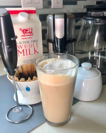 A customer review photo of the Zulay Original Milk Frother next to a frothy cup of coffee