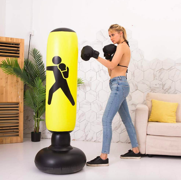 An adult using the inflatable punching bag in their living room. It is almost as tall as they are. 