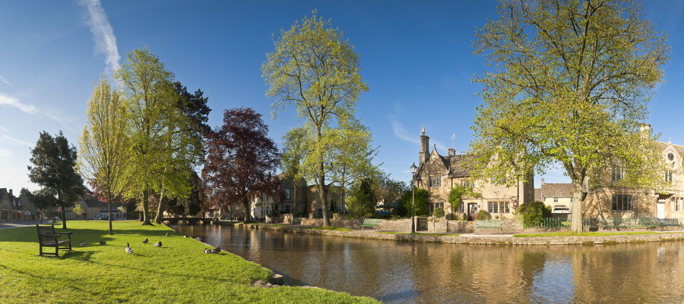 A view of the village&#x27;s stone houses from over the River Windrush on a sunny and clear day