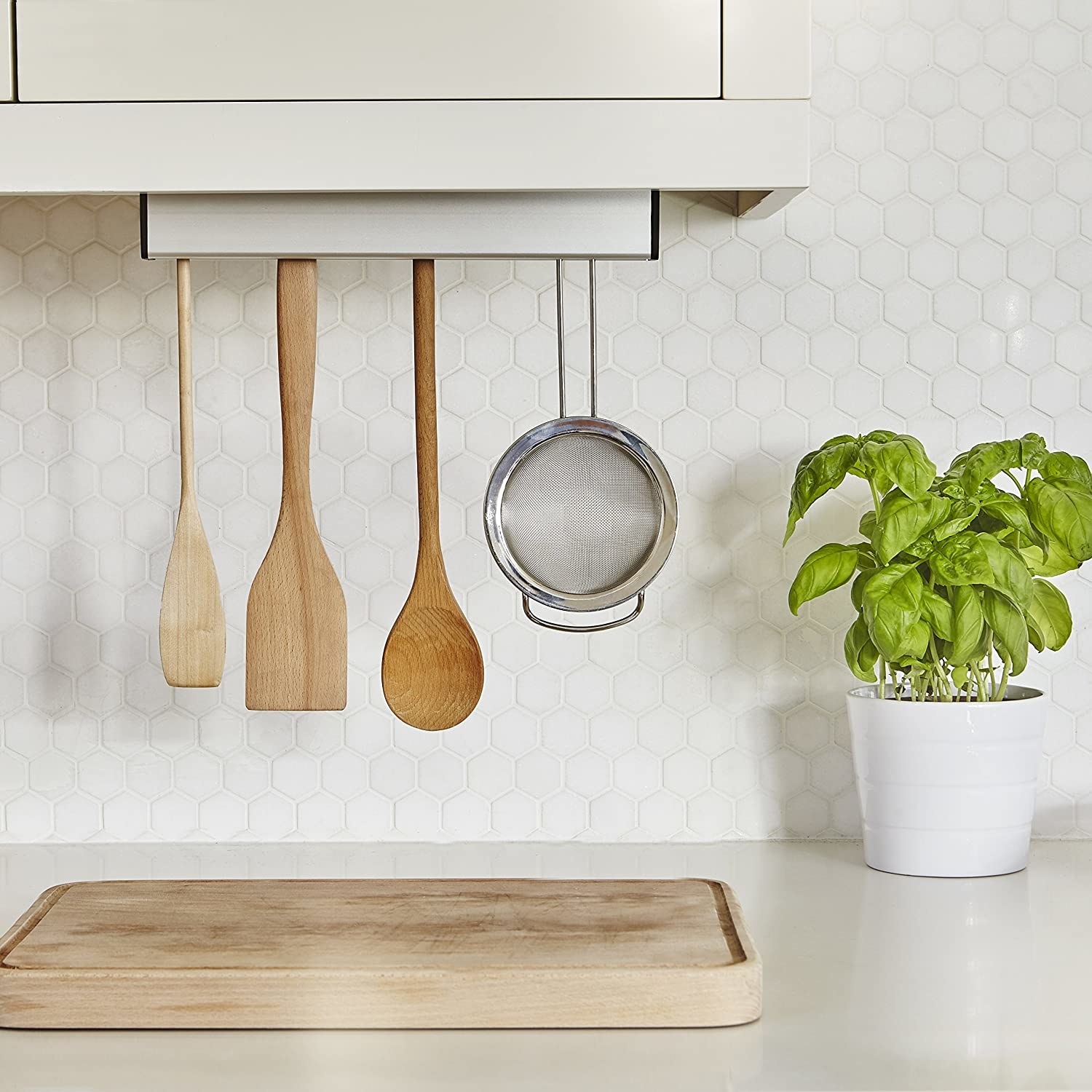 The utensil holder mounted under a cabinet and filled with wooden utensils and a stainless steel strainer