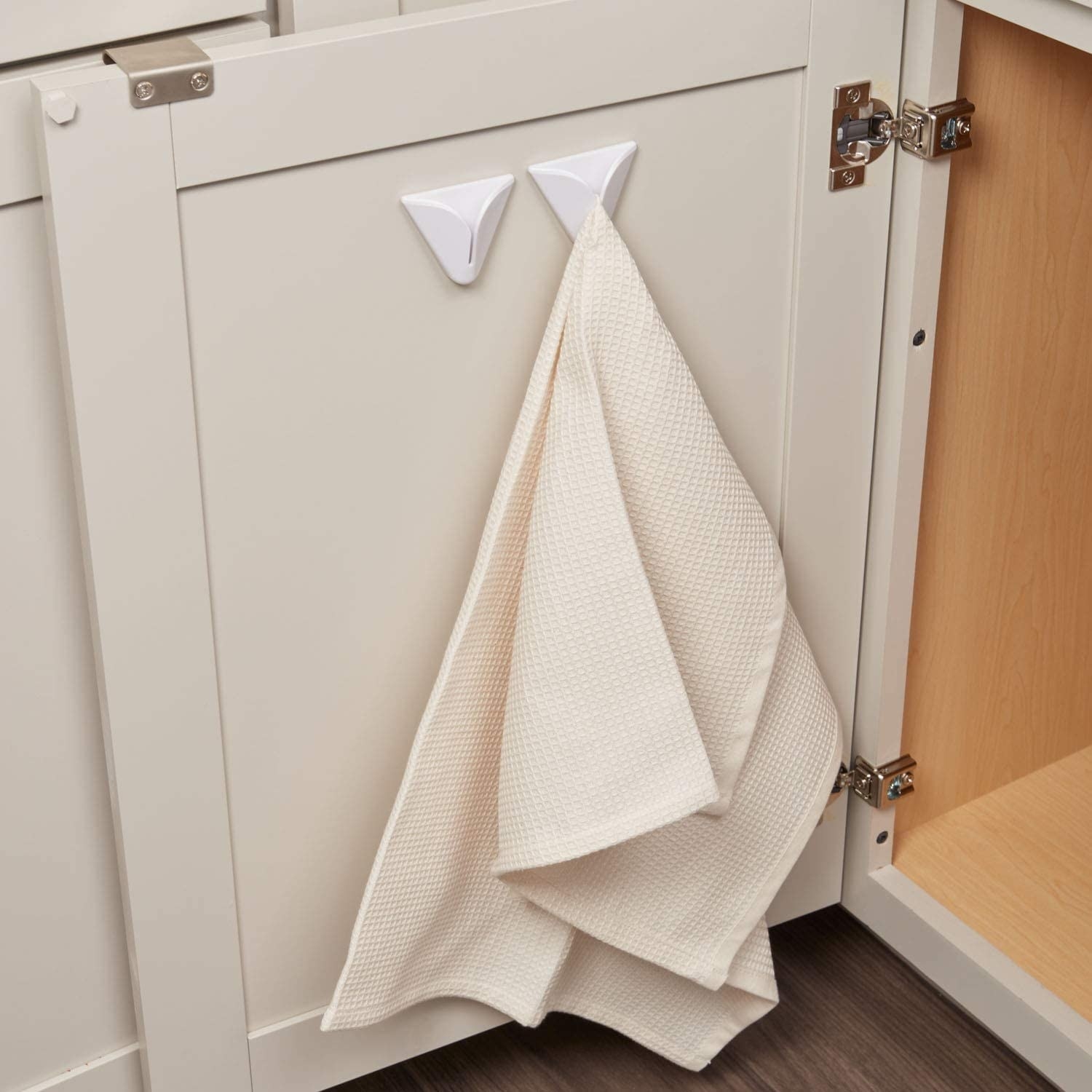 An open cabinet door with the two hooks installed on the inside and holding tea towels