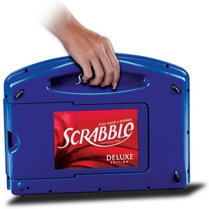 Model's hand holding the closed blue Scrabble board by its handle