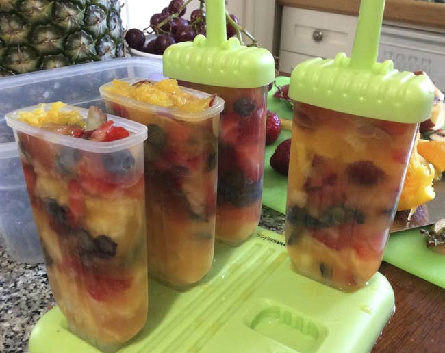 four ice pop containers filled with the fruit mix. Two have the tops on them that will serve as the sticks