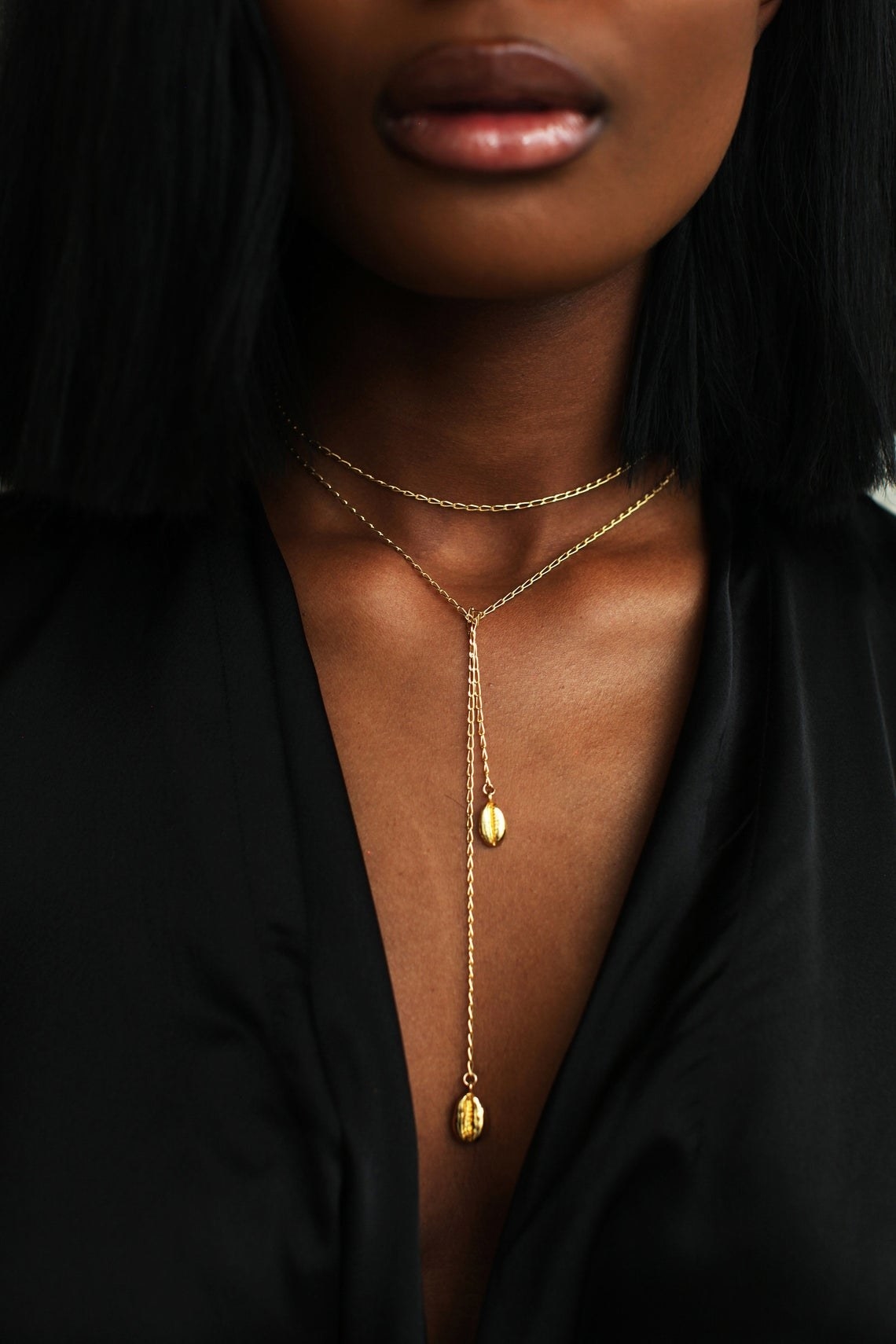 A model wearing the gold necklace. It has two cowrie shells in gold on either end and a long chain that can be worn around the neck or cascading down the chest 