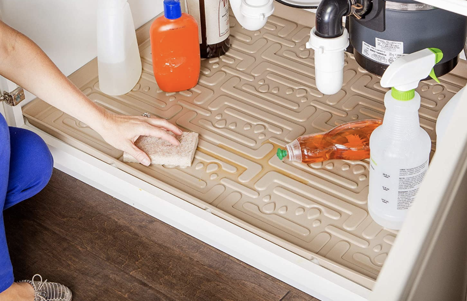 A model cleaning the grooves of the mat under a sink