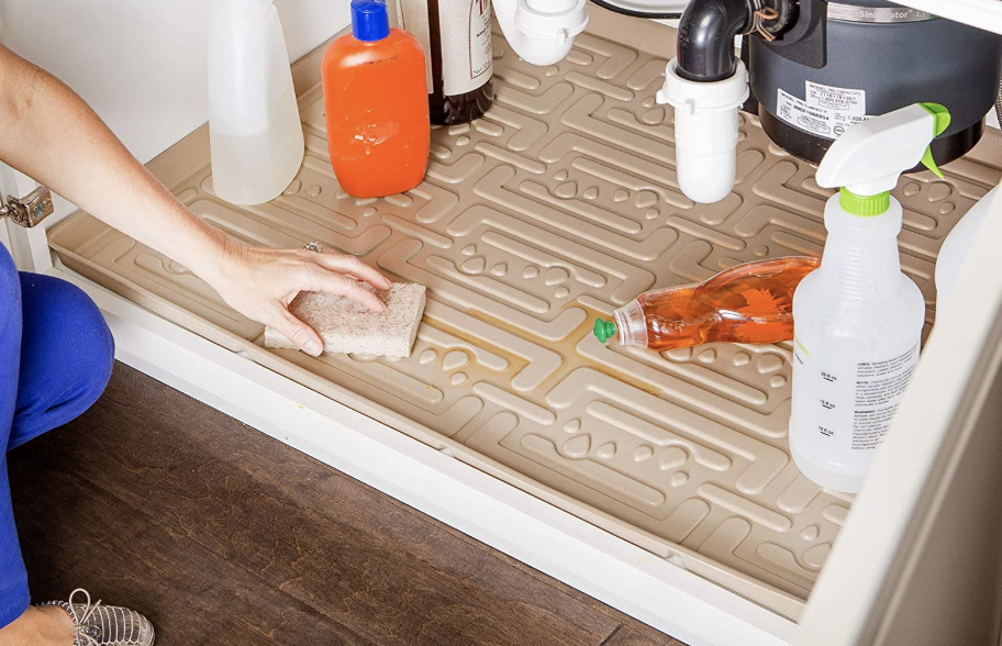 A model cleaning the grooves of the mat under a sink 