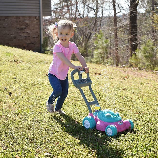 a child pushing the pink and teal blue lawn mower as bubbles rise from it