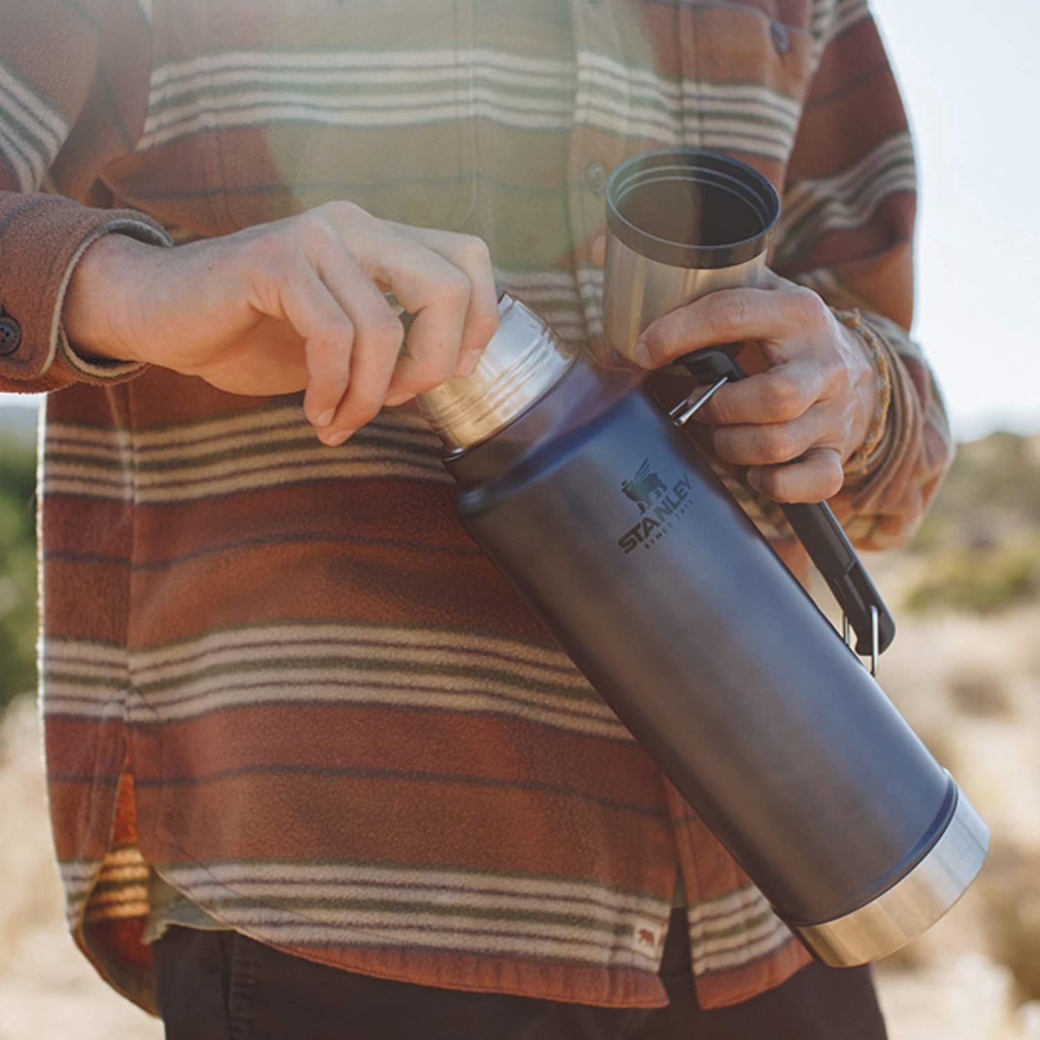 person in the outdoors opening a tall thermos