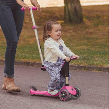 a young child sitting on the scooter being pushed by an adult