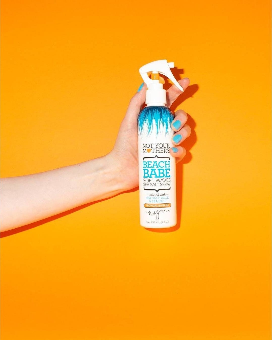 A hand holding up a spray bottle of the product