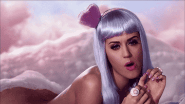 GIF of Katy Perry laying on a cloud nude with a purple wig from her &quot;California Gurls&quot; music video