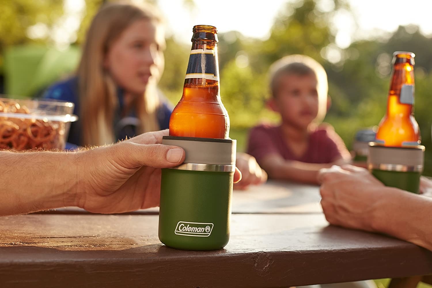 People sit at a picnic table with a bottle in a coozie