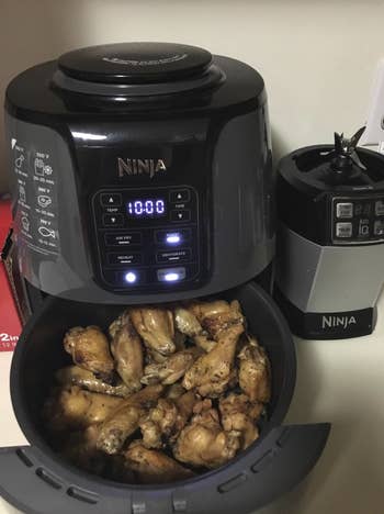 An air fryer with its drawer pulled out and fried chicken wings sitting inside