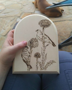A reviewer holding an arched piece of wood with an engraving of two birds resting on plant stems