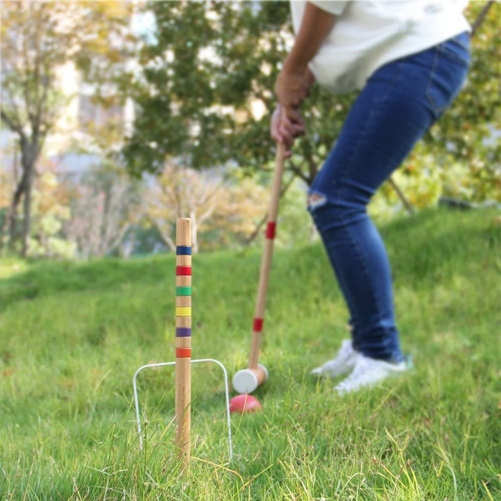 A model playing croquet with a wooden mallet and a multi-colored wooden stake
