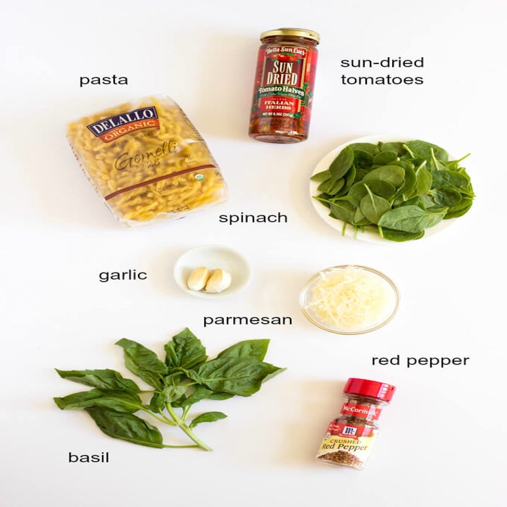 Pasta ingredients including sun dried tomatoes, spinach, pasta, garlic, Parmesan, basil, and red pepper flakes.
