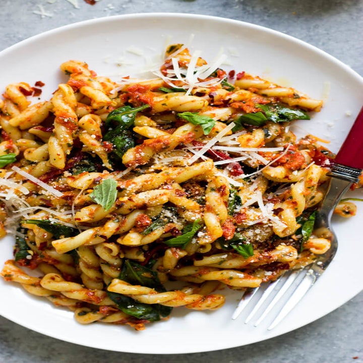 A plate of pasta with spinach, sun dried tomatoes, and shredded Parmesan cheese.