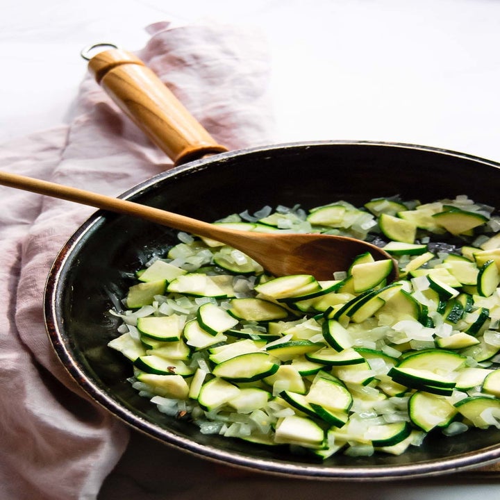 Chopped zucchini and onions cooking in a skillet.