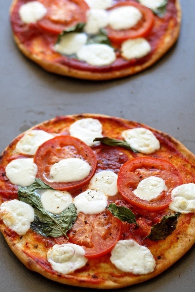 Two pizza pitas topped with sliced tomatoes, mozzarella, and basil.