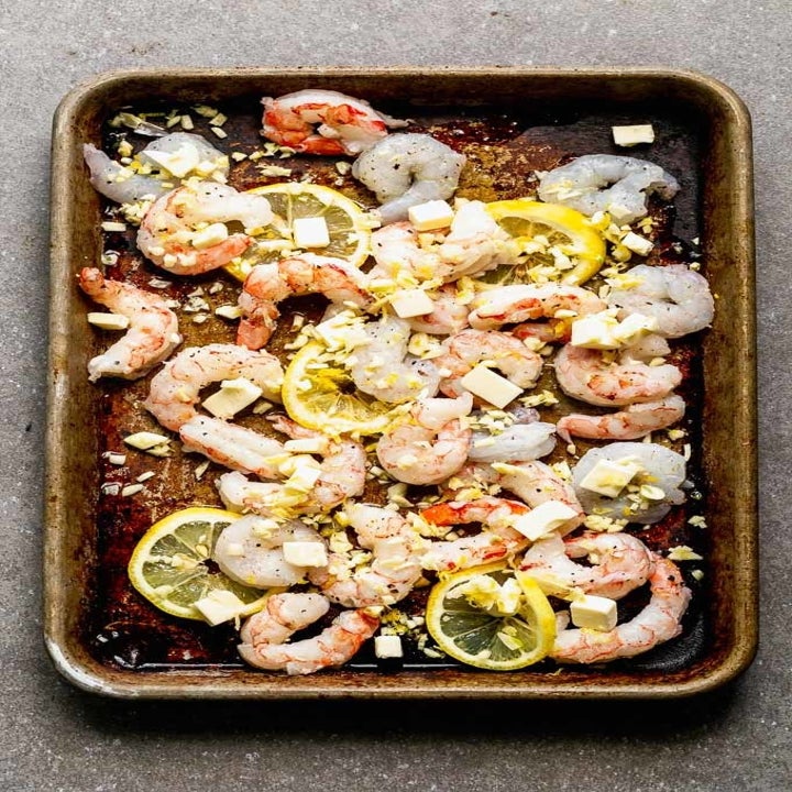Shrimp tossed with garlic, oil, and lemon on a sheet pan.
