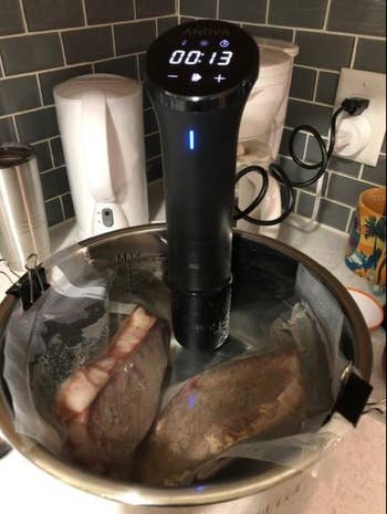 A reviewer's sous vide sits in a pot cooking two steaks