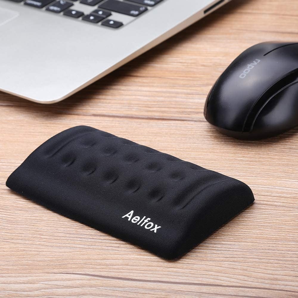 A wrist rest behind a computer mouse on a desk