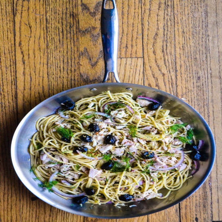 A top-down shot of spaghetti with tuna, olives, and dill in a skill.